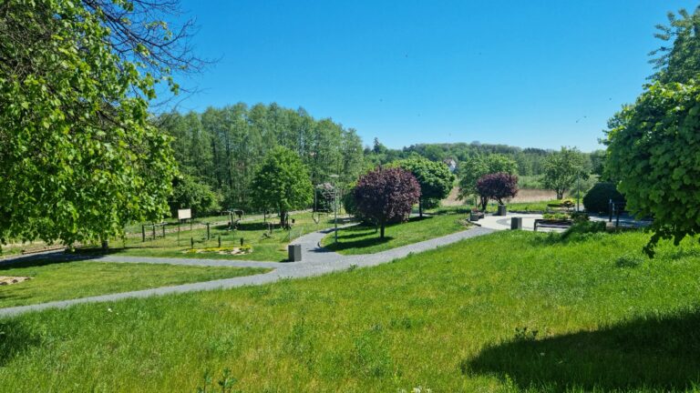 Park z alejkami i ławkami na terenie osiedla, w tle las
